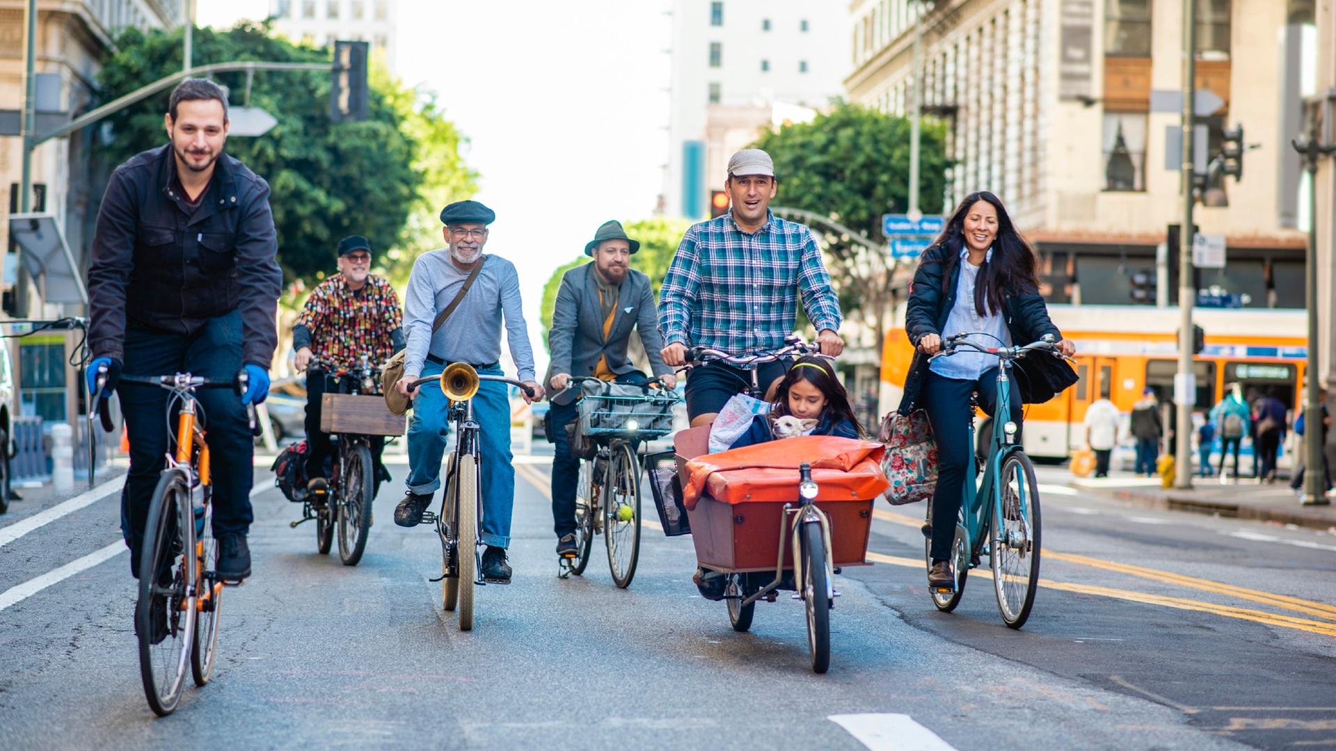 Fahrradfahrerinnen und Lastenradfahrer mit Kind und Hund auf einer Straße in Downtown Los Angeles.