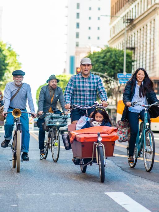 Fahrradfahrerinnen und Lastenradfahrer mit Kind und Hund auf einer Straße in Downtown Los Angeles.