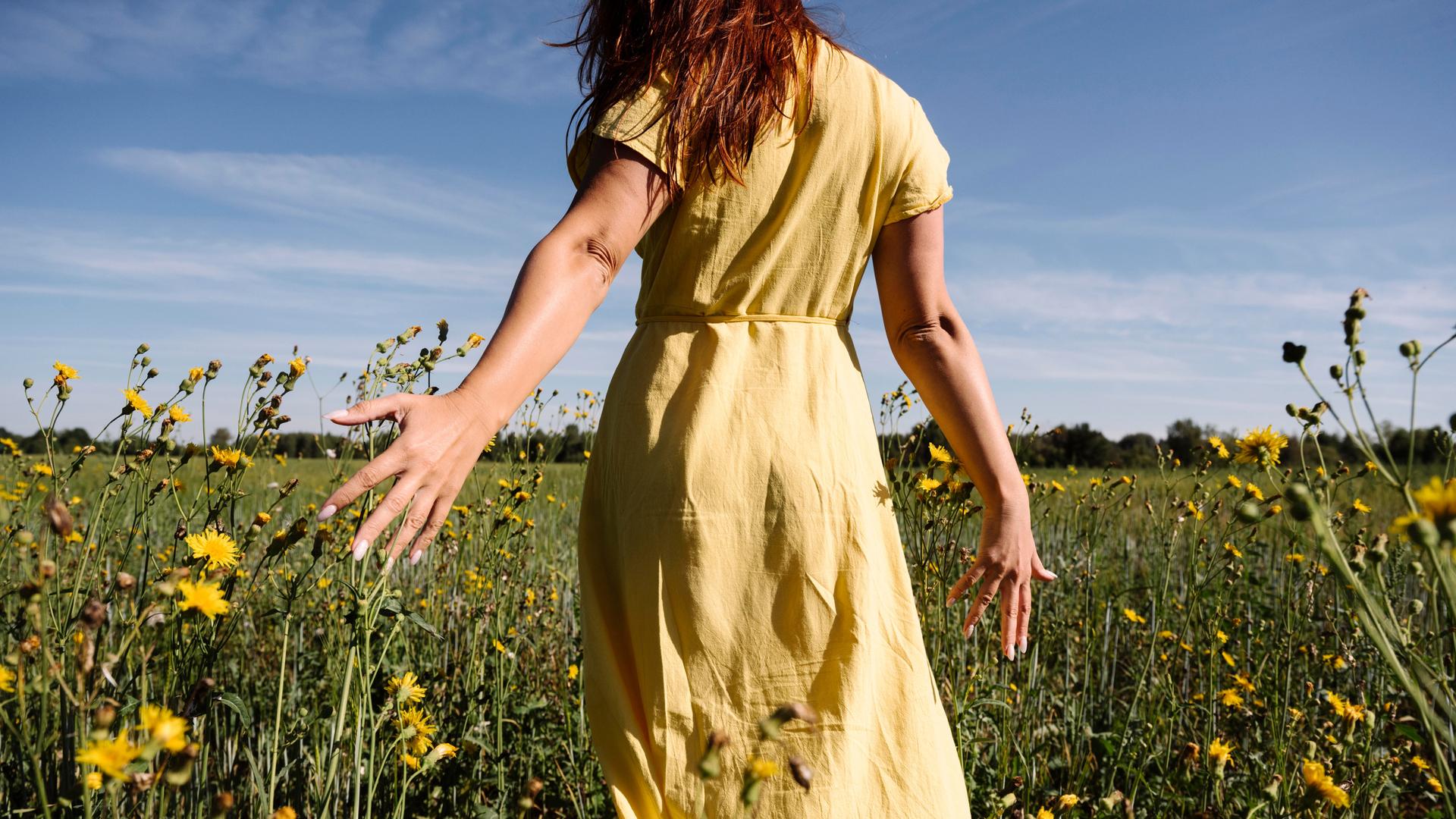 Fau im gelben Kleid läuft über eine Blumenwiese. 