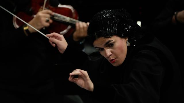 Paniz Faryousefi hält ihren Kopf schräg und schaut sehr aufmerksam. Ihre Hände sind in der Luft. In der rechten Hand hält sie einen Dirigenten-Stab.