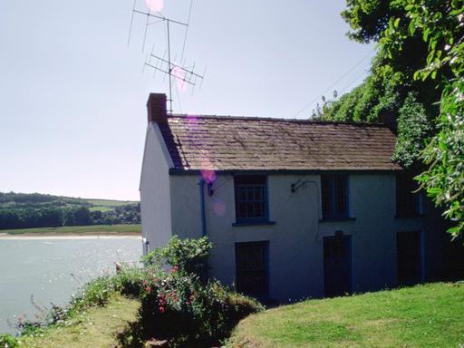 Ein Bootshaus mit einer Antenne drauf steht am Wasser. Durch einen Rasen bewachsenen Garten führt ein Weg zum Haus. Ein Bootshaus mit einer Antenne drauf steht am Wasser. Durch einen Rasen bewachsenen Garten führt ein Weg zum Haus.
