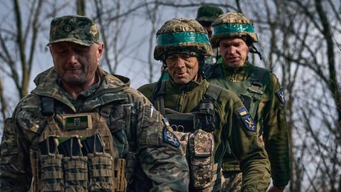 Vier Soldaten in grün-beigen Uniformen gegen hintereinander. Im Hintergrund unscharf Bäume.