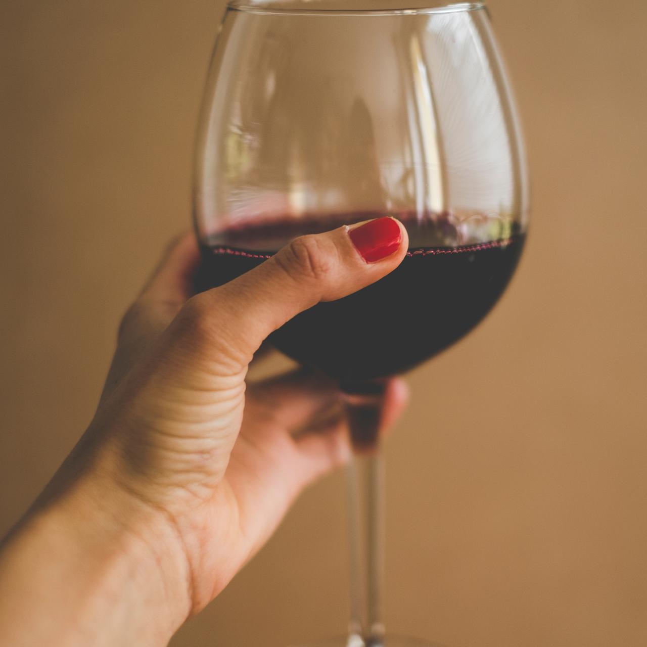 Eine weibliche Hand hält ein Glas Rotwein.