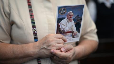 Nahaufnahme einer Frau, die ein Foto von Papst Franziskus in den Händen hält und an sich drückt.