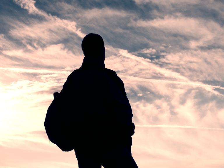 Ein namenloser Mann im Nirgendwo unterwegs. Zu sehen: Ein Mann steht mit dem Rücken zur Kamera und schaut in die Wolken. 