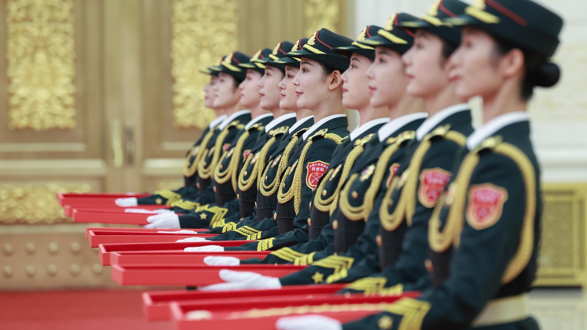 Abgebildet sind mehrere chinesische Frauen in Uniformen, die rote Schachteln in ihren Händen halten.