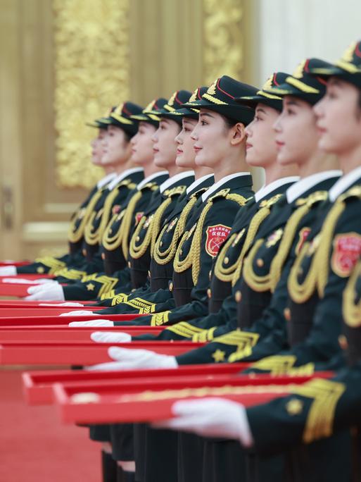 Abgebildet sind mehrere chinesische Frauen in Uniformen, die rote Schachteln in ihren Händen halten.