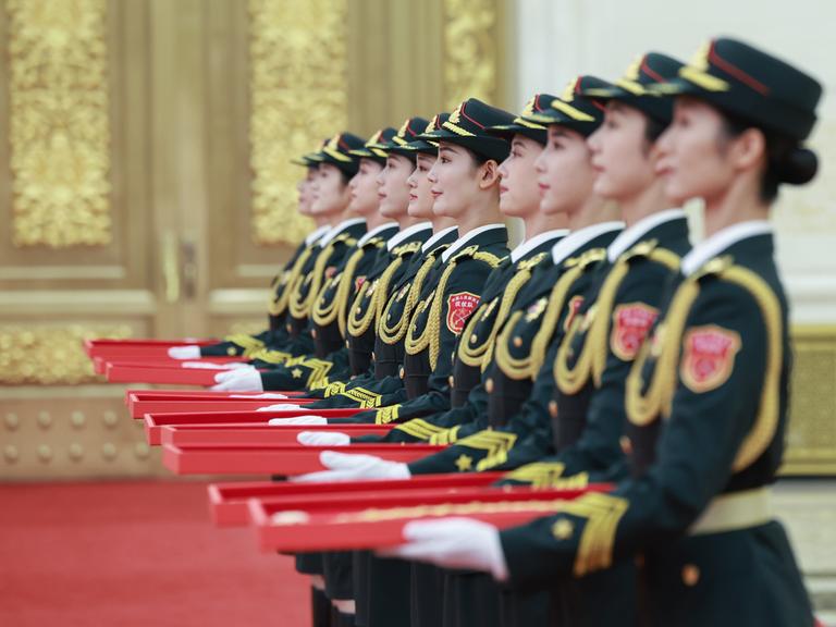 Abgebildet sind mehrere chinesische Frauen in Uniformen, die rote Schachteln in ihren Händen halten.