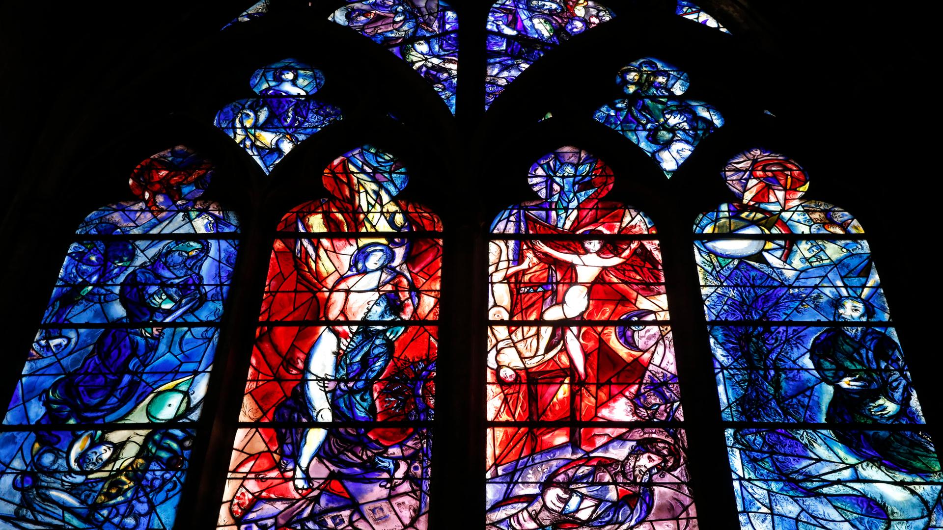 In der Kathedrale von Metz ist ein farbiges Glasfenster zu sehen. Das Fenster ist in vier große und mehrere kleine Teile unterteilt. Auf den großen Fenstern sind fragmentarisch Personen in Bewegung zu erkennen.