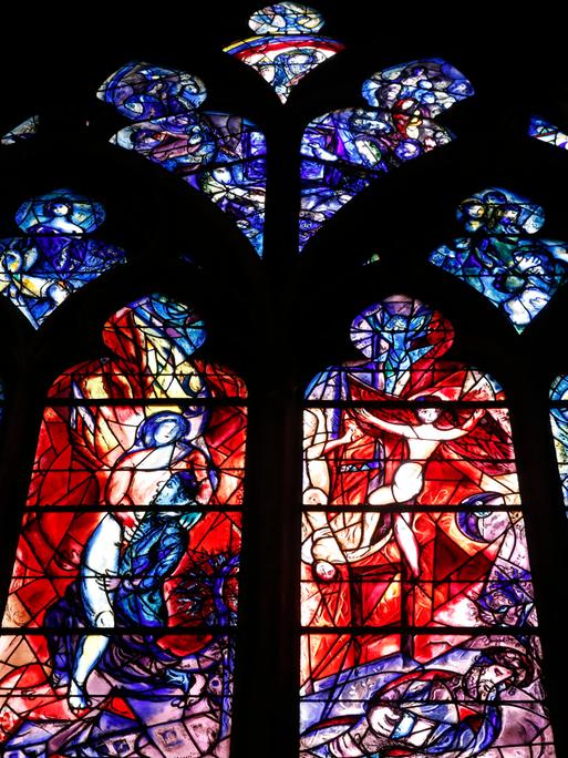 In der Kathedrale von Metz ist ein farbiges Glasfenster zu sehen. Das Fenster ist in vier große und mehrere kleine Teile unterteilt. Auf den großen Fenstern sind fragmentarisch Personen in Bewegung zu erkennen.