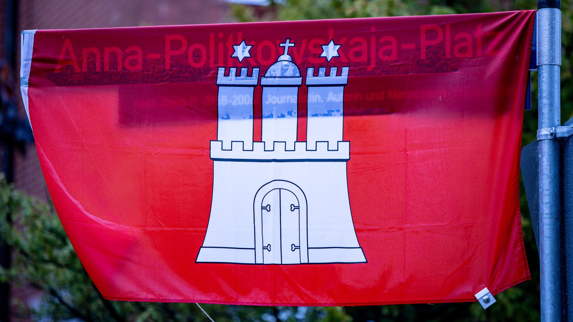 Ein in eine Flagge Hamburgs gewandetes Straßenschild mit dem Aufdruck Anna-Politkowskaja-Platz.