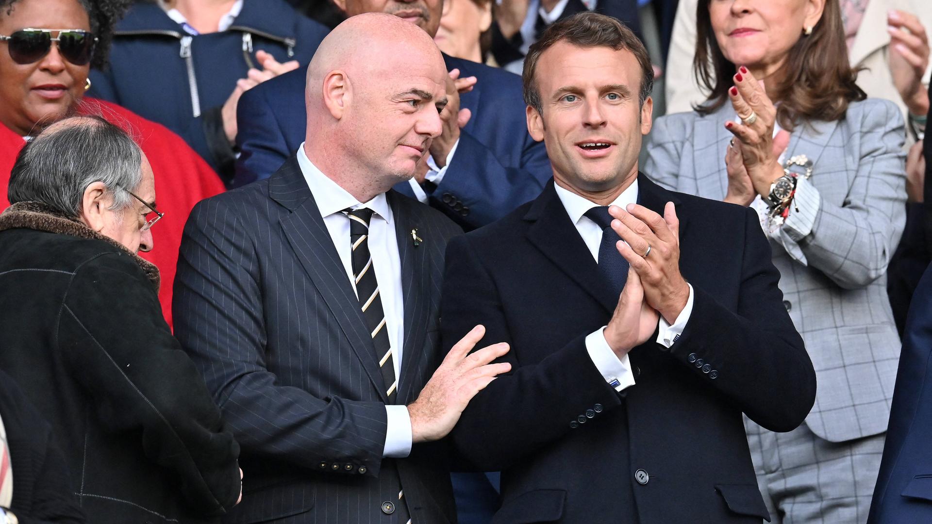 FIFA-Präsident Gianni Infantino steht auf der Tribüne eines Fußballstadions neben Frankreichs Präsident Emmanuel Macron.