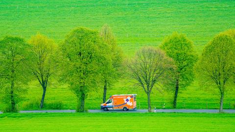 Ein Rettungswagen fährt auf einer Alle durch grüne Wiesen