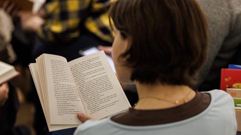 Eine Frau mit dunklen Haaren ist von hinten zu sehen. Sie hält ein Buch in der Hand und liest. 