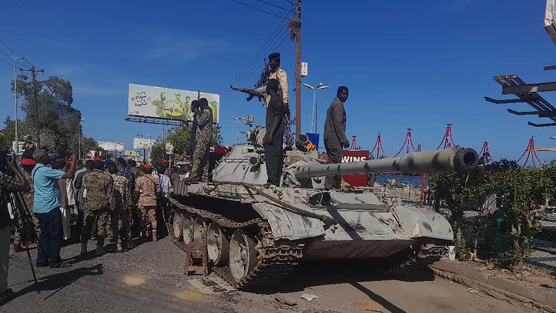 Bewaffnete Männer in Militärjacken stehen auf einem Panzer.