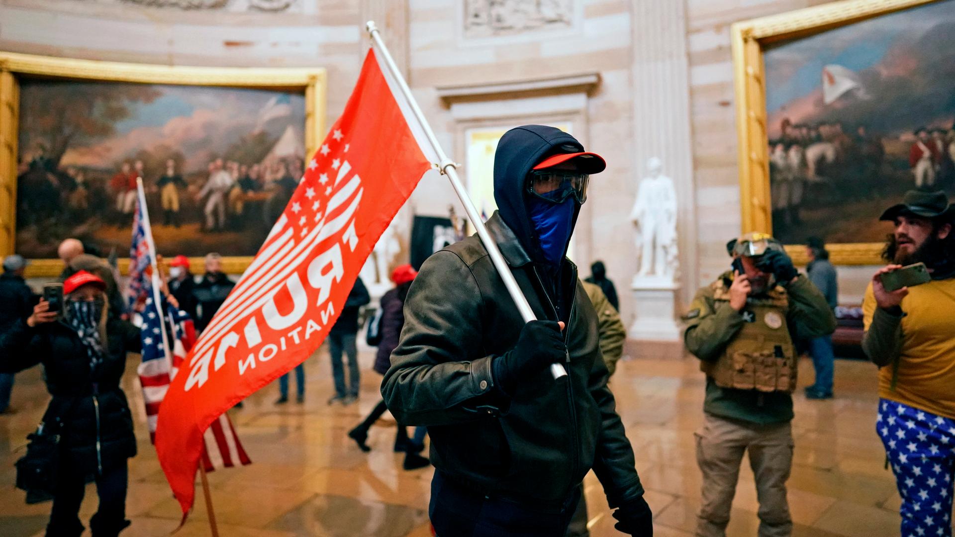 Eine vermummte Person steht mit Trump-Flagge im Capitol