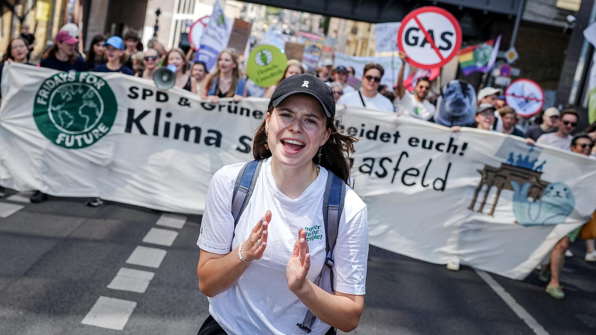 Luisa Neubauer läuft über eine Straße in Berlin, hinter ihr halten Klimaaktivisten ein Banner hoch.