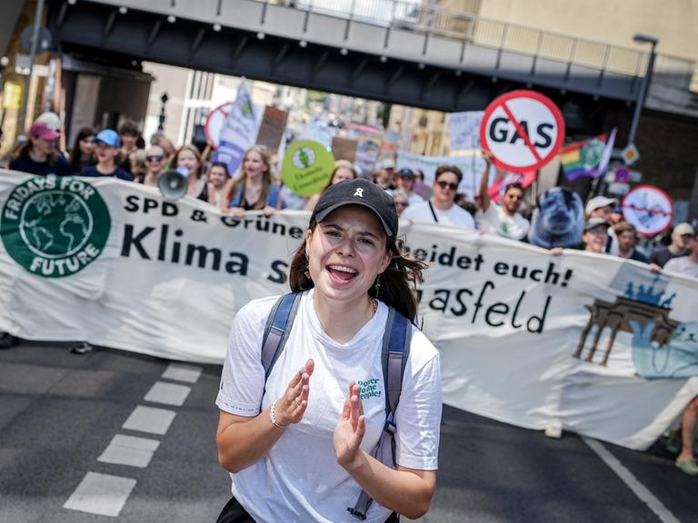 Luisa Neubauer läuft über eine Straße in Berlin, hinter ihr halten Klimaaktivisten ein Banner hoch.