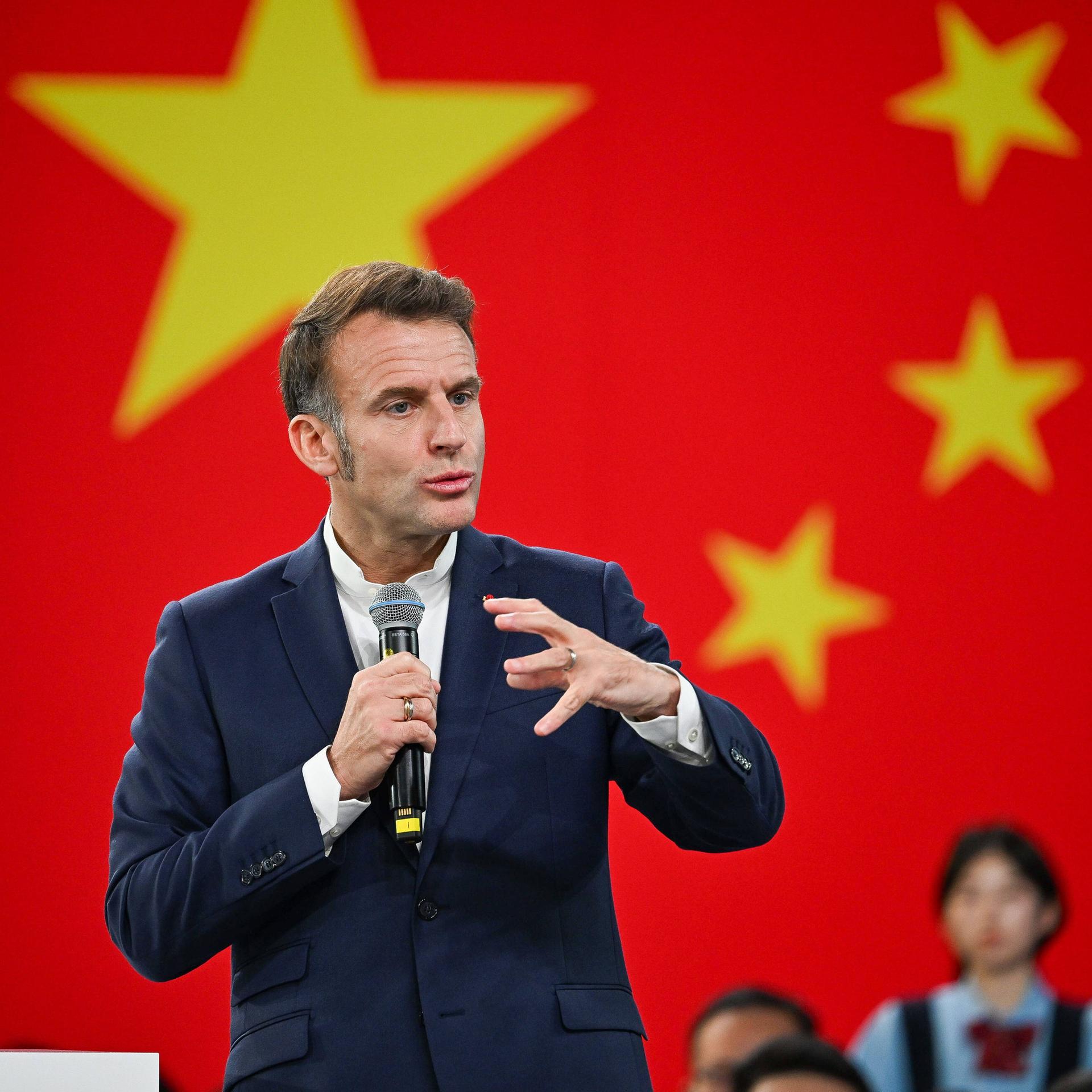 Frankreichs Präsident Emmanuel Macron spricht vor Studenten bei einem China-Besuch. Hinter ihm ist die chinesische Landesflagge. 