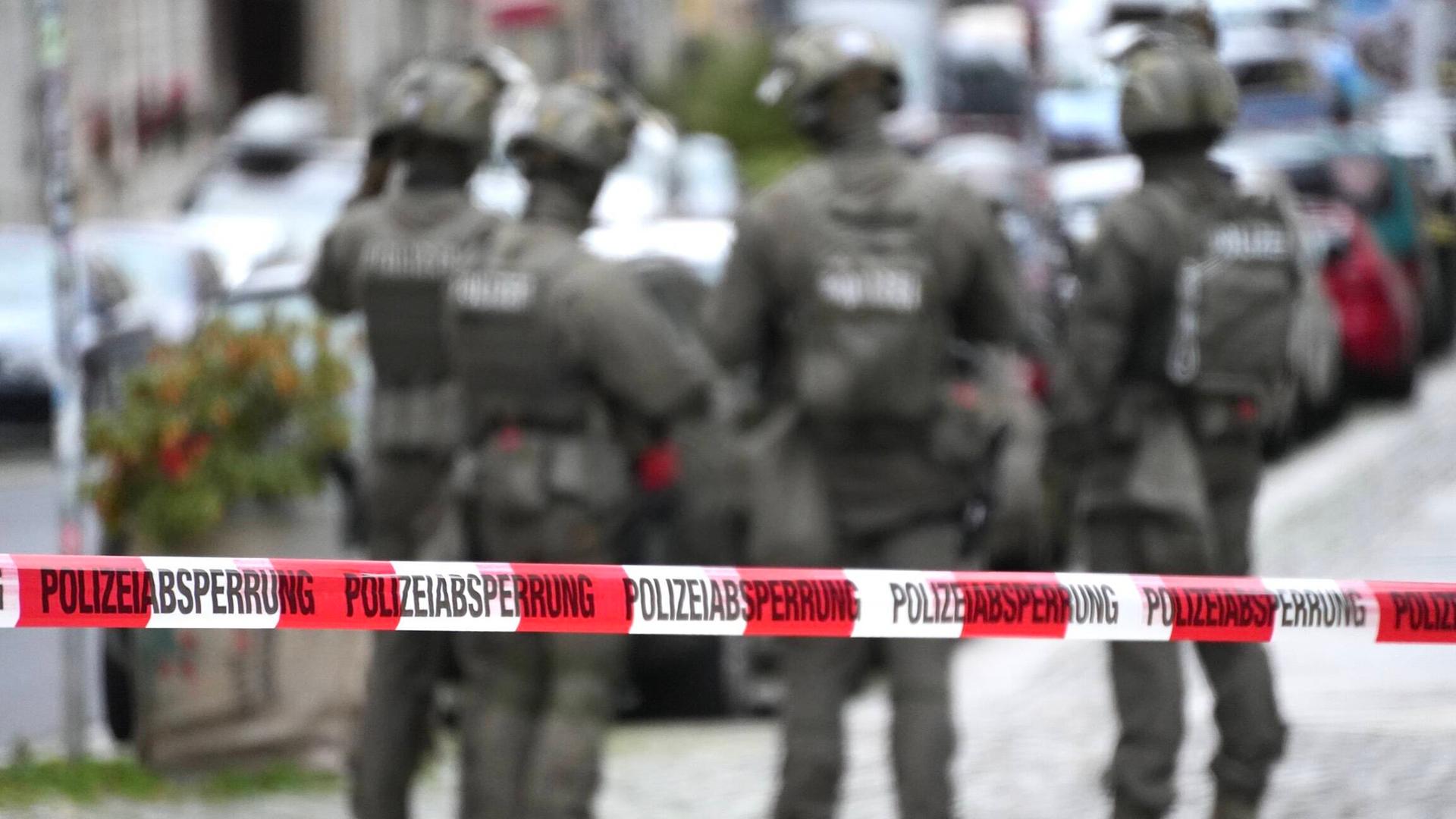 Verschwommene Polizisten des SEK Dresden. Davor eine Polizeiabsperrung. (Archivbild)