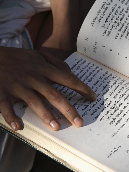 Eine Person hält ein offenes Buch in der Hand, in dem Verse auf Sanskrit stehen. Eine Person hält ein offenes Buch in der Hand, in dem Verse auf Sanskrit stehen.