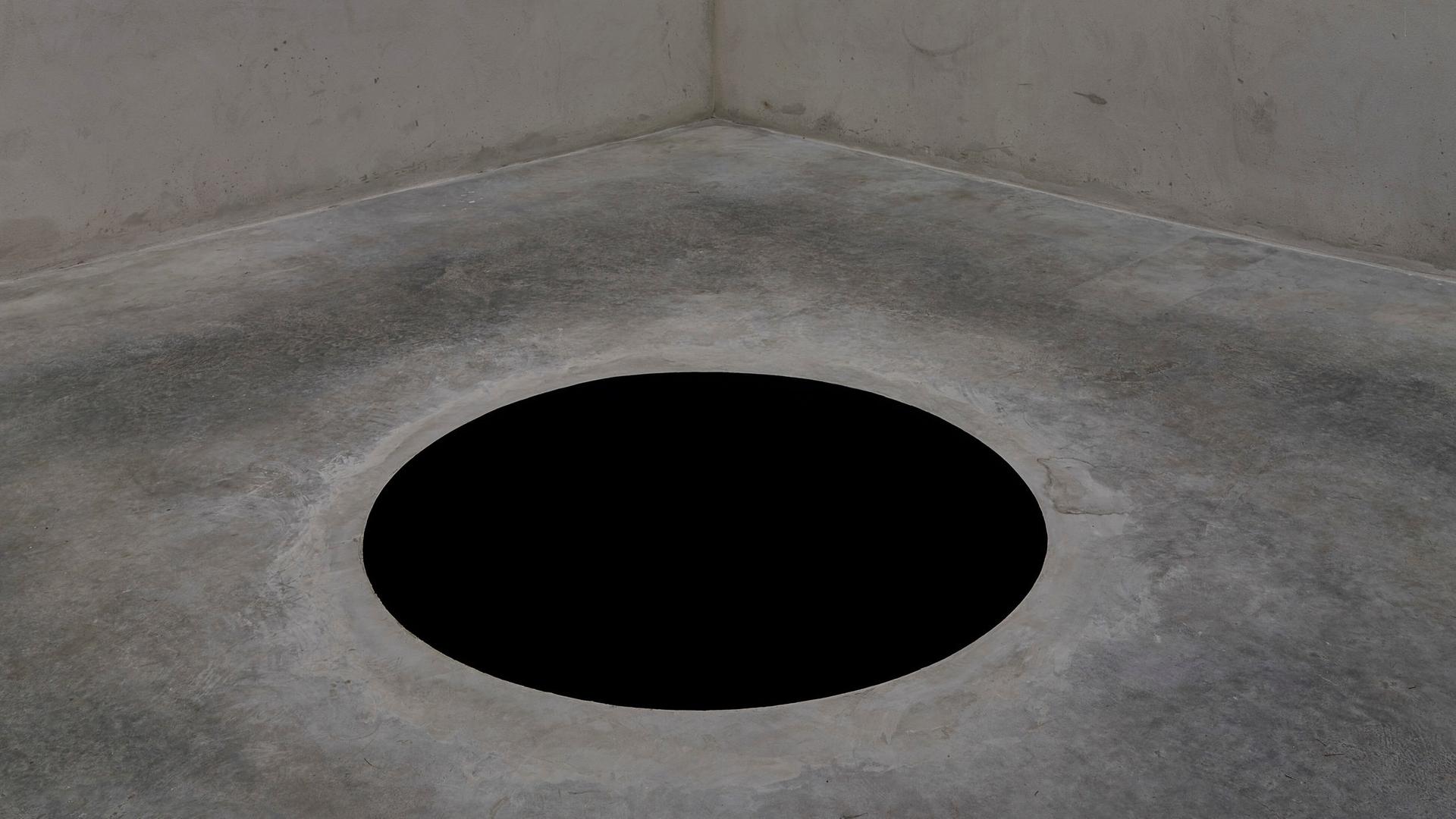 Ein 2,5 Meter tiefes schwarzes Loch ist auf einem grauen Boden in einem Museum zu sehen. Es ist ein Werk des Künstlers Anish Kapoor. Ein 2,5 Meter tiefes schwarzes Loch ist auf einem grauen Boden in einem Museum zu sehen. Es ist ein Werk des Künstlers Anish Kapoor.