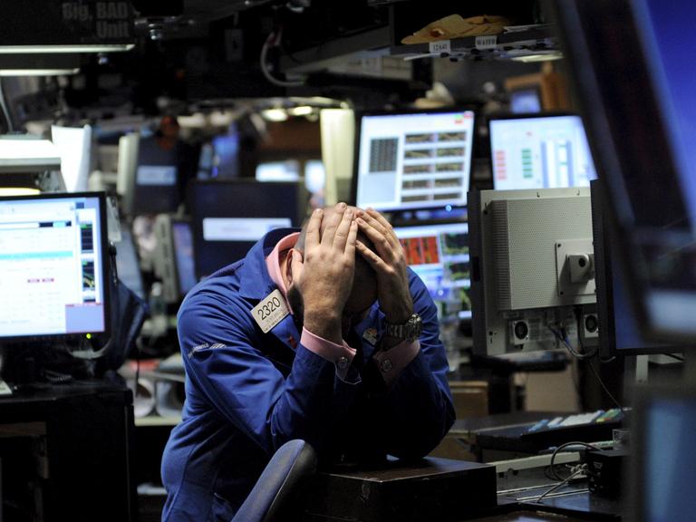 Ein Händler an der Börse, umringt von Monitoren, hält sich aus Verzweiflung den Kopf.