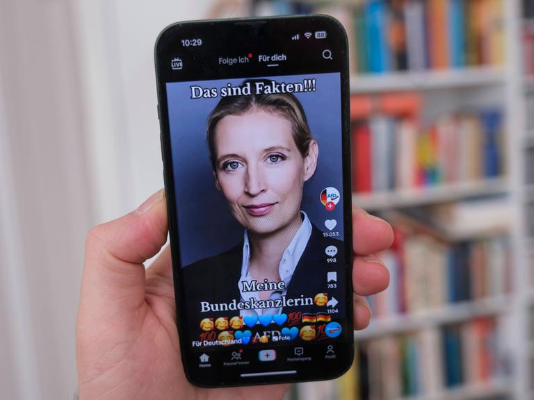 Hand hält ein Mobiltelefon auf dessen Display die Seite der AFD Politikerin Alice Weidel auf Plattform TikTok zu sehen i