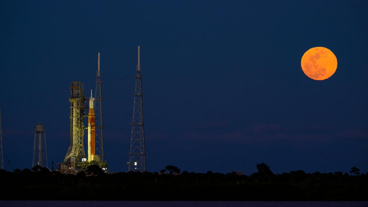 Nachthimmel am 01.02.2026 über Cape Canaveral in Florida. Links im Bild eine senkrecht stehende Orion-Rakete, rechts im Bild ein orangefarbener Vollmond.