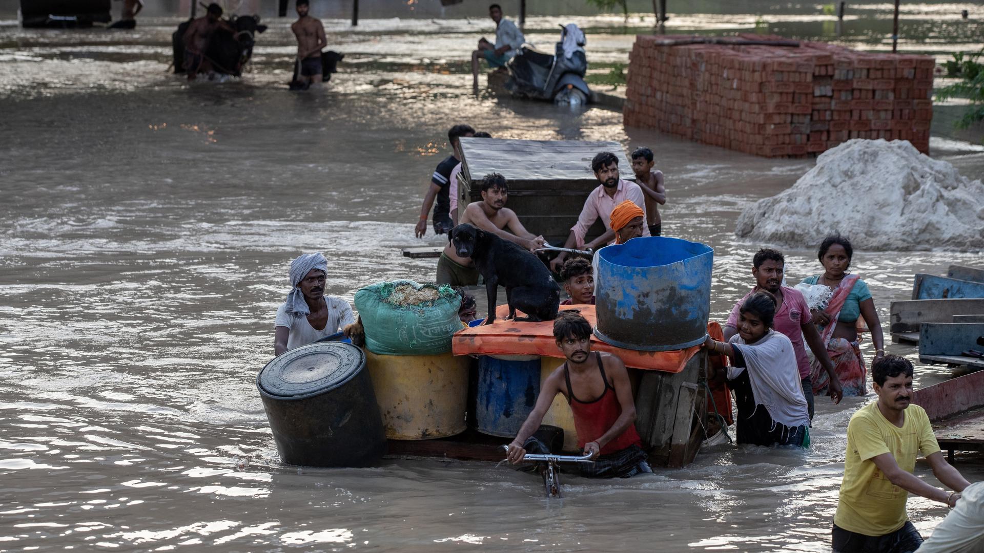 In Indien schieben Menschen ihr Hab und Gut mit einem Lastenfahrrad durch eine überflutete Straße. In Indien schieben Menschen ihr Hab und Gut mit einem Lastenfahrrad durch eine überflutete Straße.
