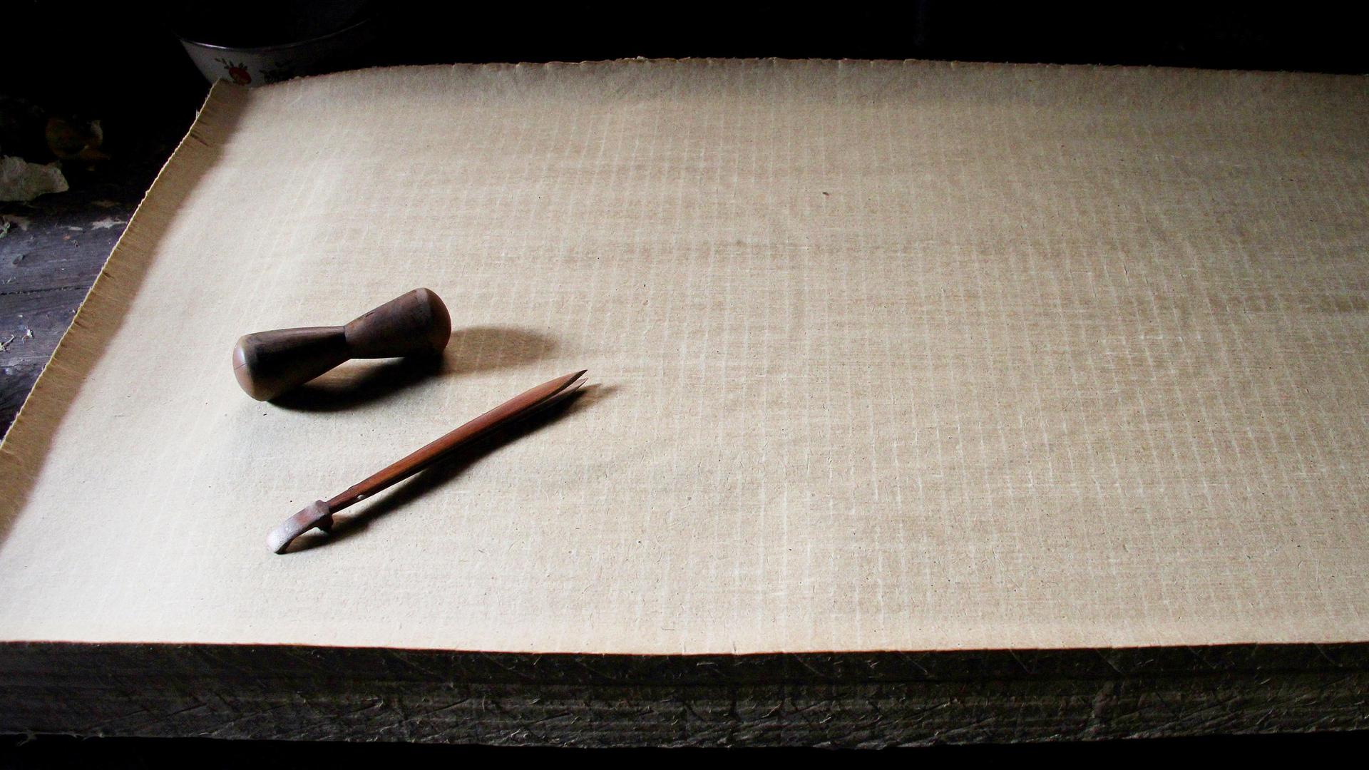 Ein Stapel Papier, darauf liegt eine Feder und Tinte: Es handelt sich um handgemachtes Papier aus China.