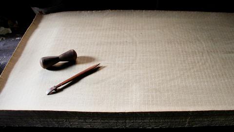 Ein Stapel Papier, darauf liegt eine Feder und Tinte: Es handelt sich um handgemachtes Papier aus China.