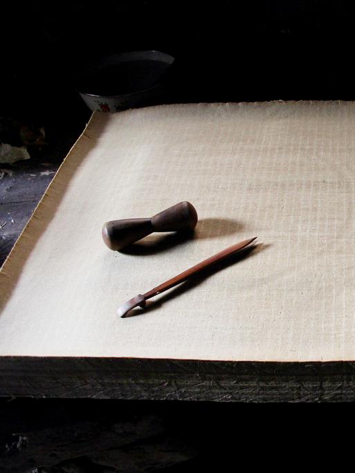 Ein Stapel Papier, darauf liegt eine Feder und Tinte: Es handelt sich um handgemachtes Papier aus China.