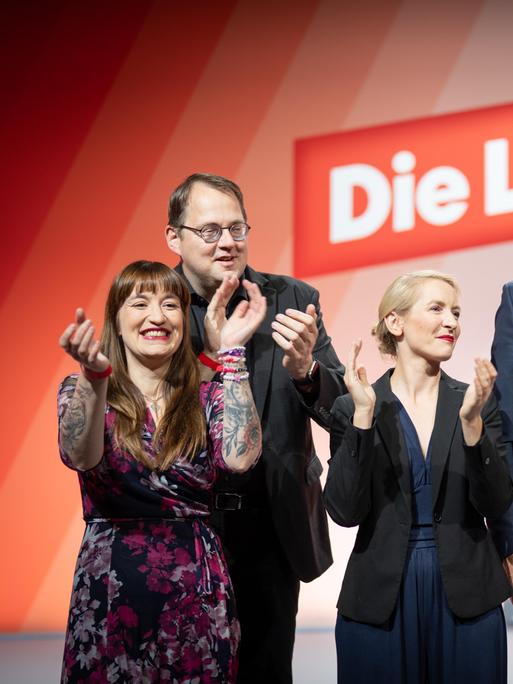 Die Linken-Politiker Heidi Reichinnek, Sören Pellmannn, Ines Schwerdtner und Jan van Aken (von links). Sie wirken ausgelassen, im Hintergrund ist auf roter Wand das Logo der Partei Die Linke zu sehen. 