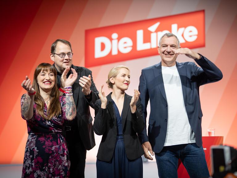 Die Linken-Politiker Heidi Reichinnek, Sören Pellmannn, Ines Schwerdtner und Jan van Aken (von links). Sie wirken ausgelassen, im Hintergrund ist auf roter Wand das Logo der Partei Die Linke zu sehen. 
