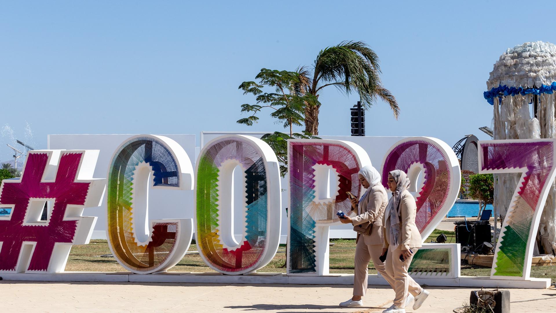 Das Logo von der Welt-Klima-Konferenz sind große Buchstaben und Zahlen "COP27". Das Logon ist vor Palmen aufgestellt.