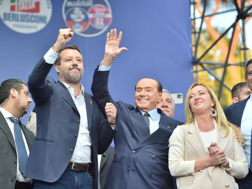 Matteo Salvini und Silvio Berlusconi heben jeweils ihre rechte Hand und stehen links neben Giorgia Meloni.
