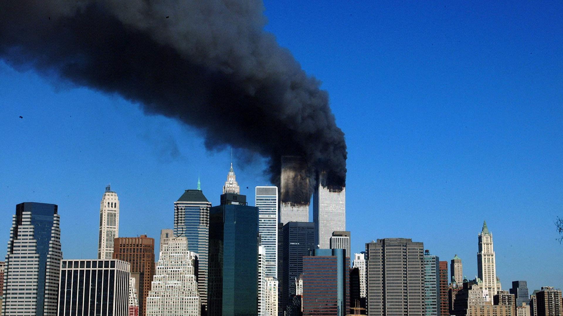 Die Silhouette der brennenden Zwillingstürme in Manhattan hebt sich vor einem blauen Himmel ab. Die Silhouette der brennenden Zwillingstürme in Manhattan hebt sich vor einem blauen Himmel ab.