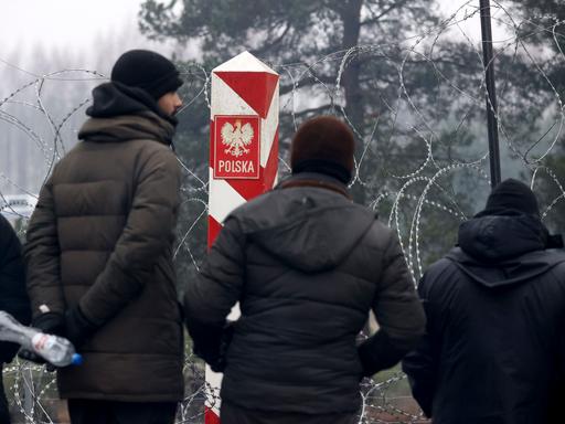 Migranten stehen in vor einem Stacheldrahtzauns und einem polnischen Grenzpfeiler an der belarussisch-polnischen Grenze in der Nähe von Grodno im  November 2021.