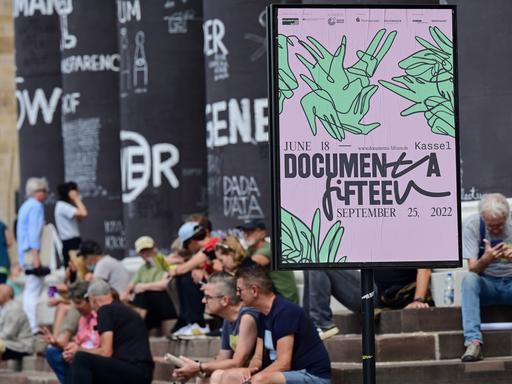 Besucher der documenta fifteen sitzen auf den Stufen des Fridericianums. Die 100 Tage währende Weltkunstausstellung feiert Halbzeit.