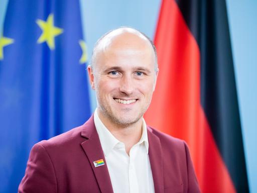 Sven Lehmann steht vor einer europäischen und einer deutschen Fahne