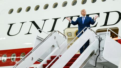 US-Präsident Trump steht vor seinem Präsidentenflieger und breitet zufrieden die Arme aus.
