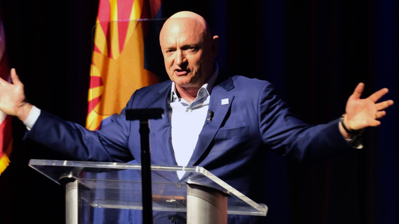 Mark Kelly steht an einem Rednerpult und streckt die Arme zur Seite.