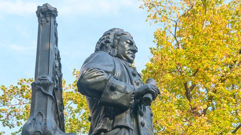 Denkmal Bachs vor der Leipziger Thomaskirche von der Seite fotografiert, sodass die Figur vor Herbslaub erscheint.