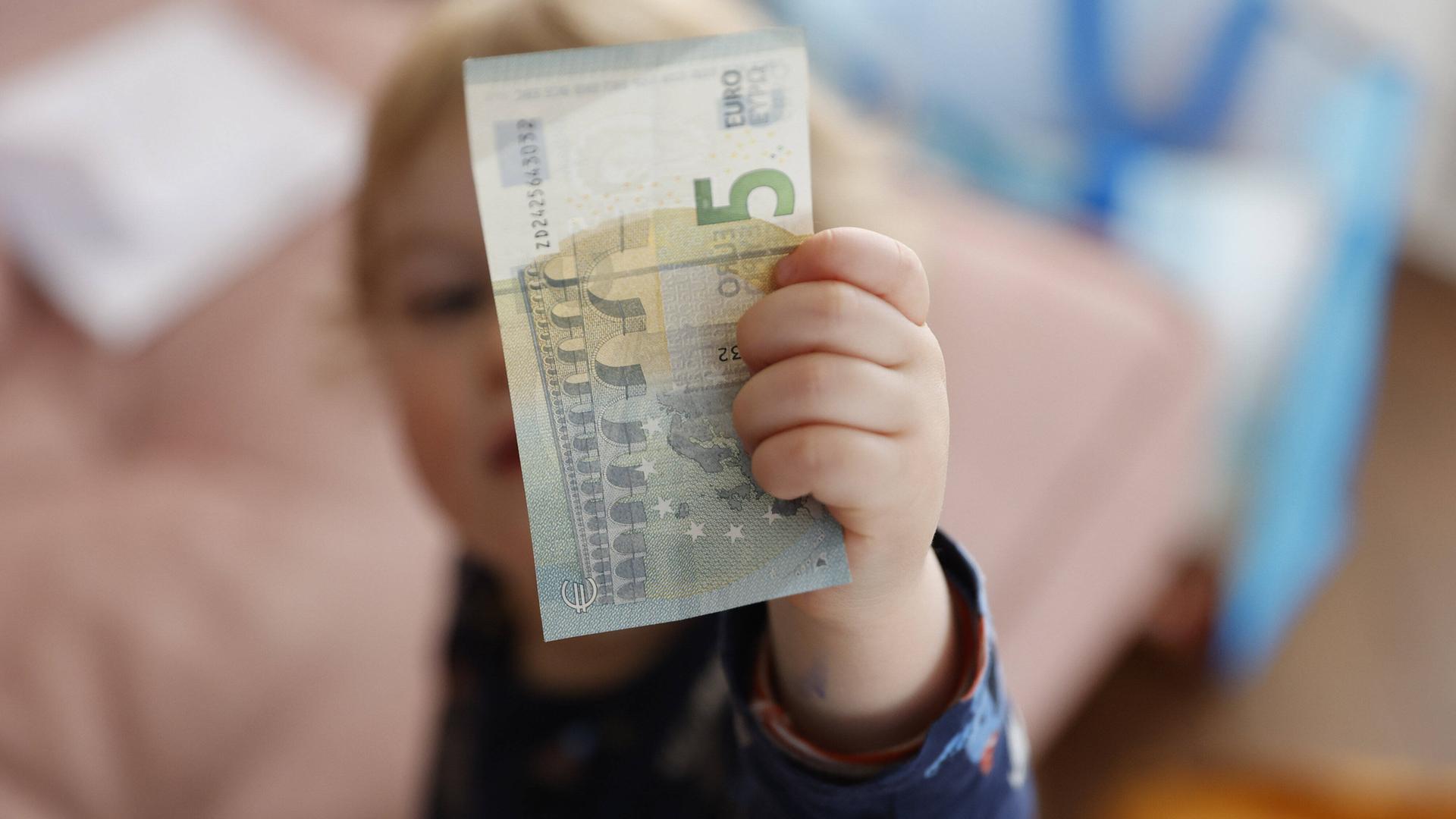 Eine Kinderhand hält einen Fünf-Euro-Schein.