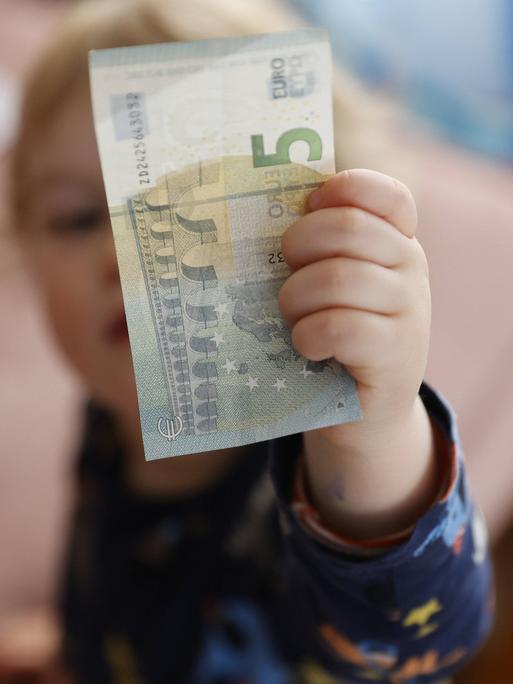 Eine Kinderhand hält einen Fünf-Euro-Schein.