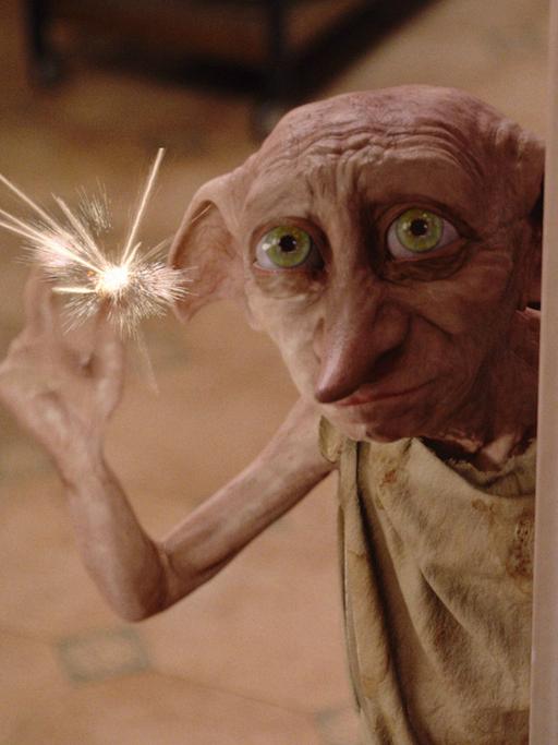 Dobby, der Hauself aus "Harry Potter" hält eine Wunderkerze in der Hand und schaut zerknittert.