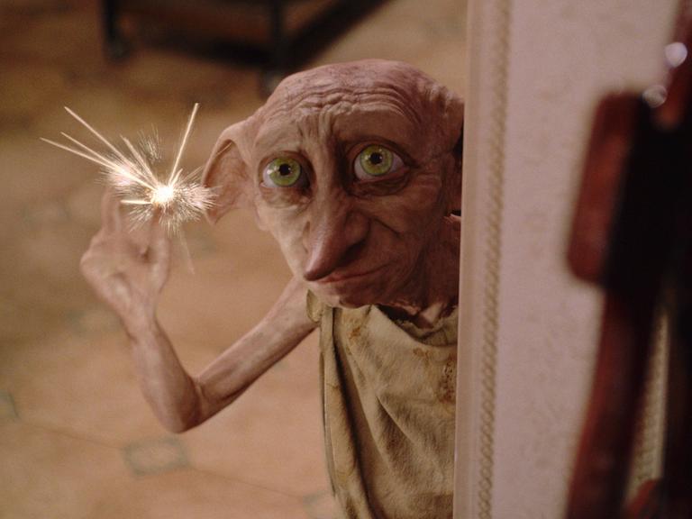 Dobby, der Hauself aus "Harry Potter" hält eine Wunderkerze in der Hand und schaut zerknittert.