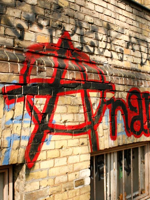 Auf einer hellbraunen Backsteinwand ist in schwarzer und roter Farbe der Schriftzug „Anarchy“ zu lesen. Auf einer hellbraunen Backsteinwand ist in schwarzer und roter Farbe der Schriftzug „Anarchy“ zu lesen.