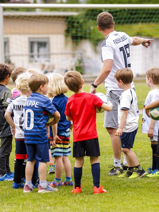 Ein ehrenamtlicher Trainer trainiert Kinder auf einem Fussballplatz